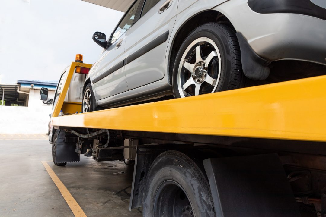 Flatbed tow truck transporting broken-down car in Corolla NC