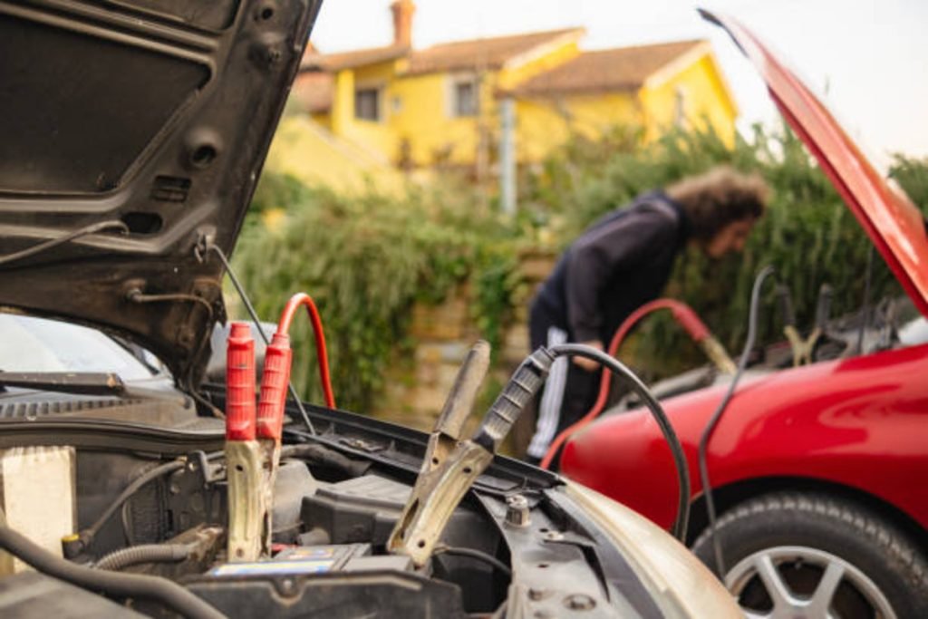 Person jump-starting a car safely with jumper cables connected to batteries.