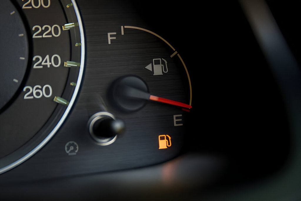Car dashboard showing the fuel gauge near empty, with the low fuel warning light illuminated.