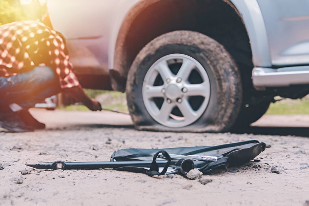 Person changing a flat tire, tools nearby, to prevent flat tires.