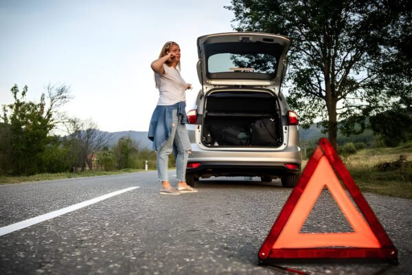 Woman stranded with car trouble, using phone near hazard triangle, needing roadside assistance