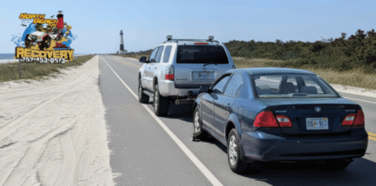 Silver SUV towing a blue sedan on a coastal road, North Beach Recovery logo visible.